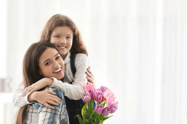 Young woman and her daughter with tulip bouquet indoors. Mother's day celebration - Foto, Bild