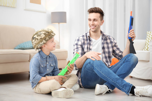 Cute boy and his father playing with toy guns at home - Photo, image