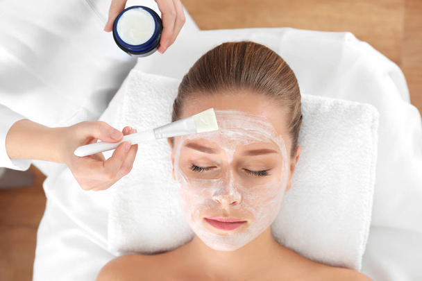 Beautician applying mask onto young woman's face in spa salon - Φωτογραφία, εικόνα