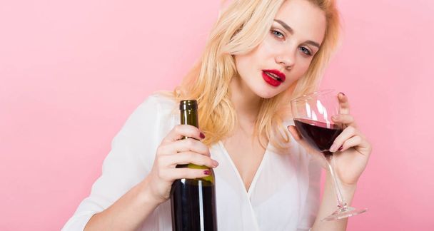 Beautiful young woman with glass and bottle of red wine on pink background - Fotografie, Obrázek