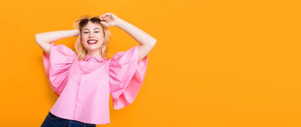 Portrait of stylish young woman in pink blouse posing on yellow background - Photo, Image