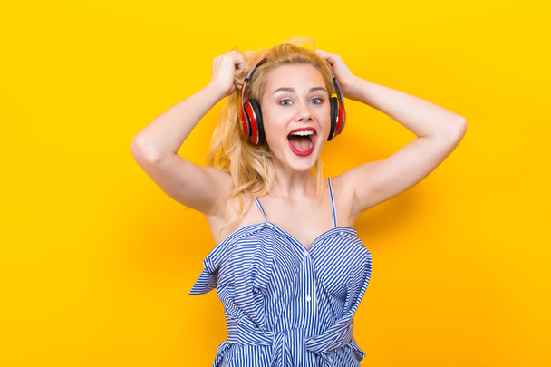 schöne emotionale junge Frau hört Musik mit Kopfhörern auf gelbem Hintergrund - Foto, Bild
