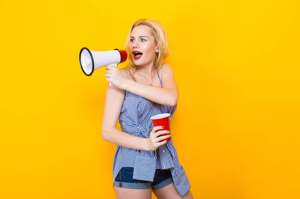 stylish young woman posing with red plastic cup and megaphone on yellow background - Fotografie, Obrázek
