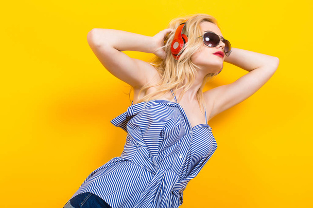 schöne emotionale junge Frau hört Musik mit Kopfhörern und tanzt auf gelbem Hintergrund - Foto, Bild
