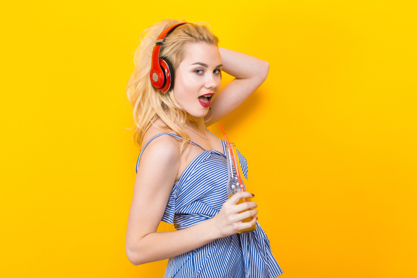 Mooie stijlvolle jongedame met rode hoofdtelefoons en verse jus d'orange op gele achtergrond - Foto, afbeelding