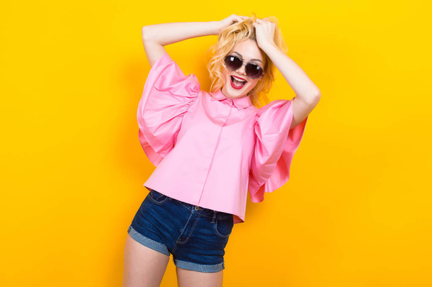 Portrait of stylish young woman in pink blouse posing on yellow background - Foto, Imagen