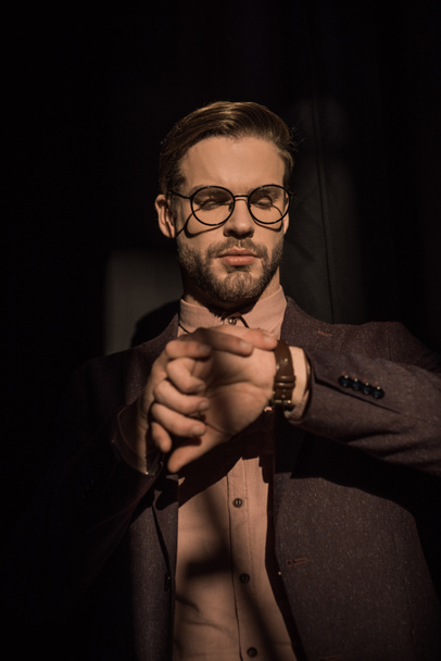 portrait of handsome stylish man in spectacles checking wristwatch - Valokuva, kuva