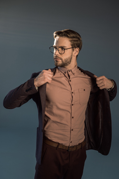 portrait of stylish man in eyeglasses wearing jacket and looking away isolated on grey - Foto, Imagen