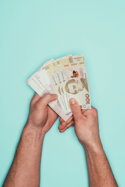 cropped shot of man holding bunch of ukrainian money isolated on turquoise - Zdjęcie, obraz