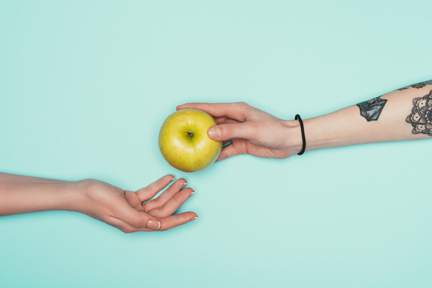 foto recortada de mujeres que pasan manzana fresca aislada en turquesa
 - Foto, imagen