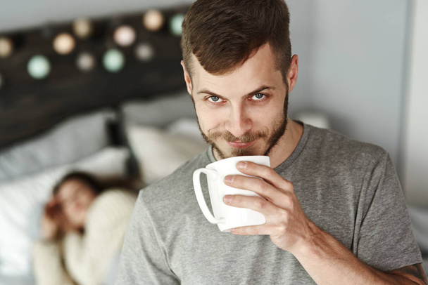 Front view of man drinking coffee in bedroom  - 写真・画像