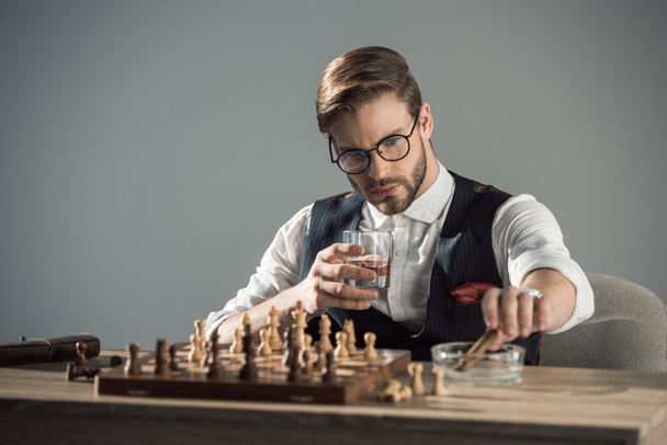 молодой бизнесмен со стаканом виски и сигарой играет в шахматы
 - Фото, изображение