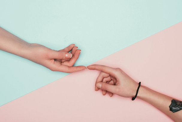 cropped shot of women touching fingers on halved pink and turquoise surface - Foto, afbeelding