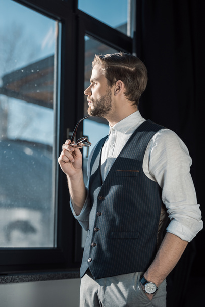 portrait of pensive young businessman holding eyeglasses and looking at window - Fotoğraf, Görsel