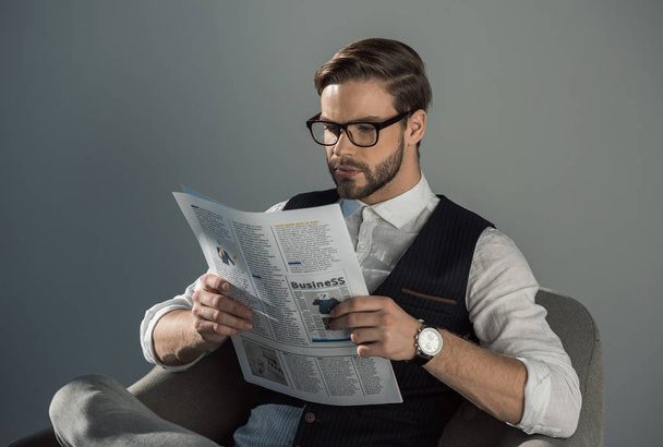 Portret van knappe jonge zakenman in brillen, het lezen van de krant geïsoleerd op grijs  - Foto, afbeelding