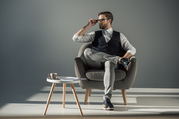 full length view of handsome stylish young man sitting in armchair and looking away - 写真・画像