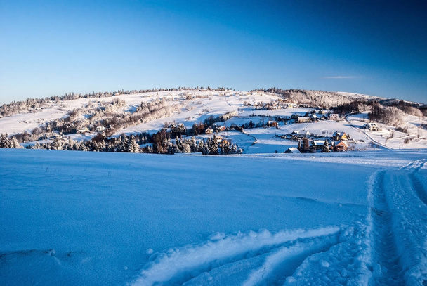 冬山田園散居集落、牧草地と木々、丘と雪し、澄んだポーランド ベスキディ山脈山脈の Koniakow の村の近くの空 - 写真・画像