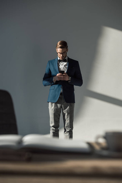 selective focus of man in eyeglasses and bow tie using smartphone  - Valokuva, kuva