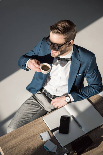 visão de alto ângulo de sorrir jovem empresário bebendo café e olhando para longe
 - Foto, Imagem