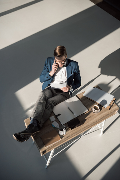 high angle view of fashionable businessman talking on smartphone while sitting at workplace  - Photo, Image