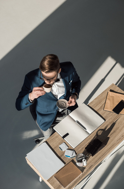 bovenaanzicht van stijlvolle jonge zakenman koffie drinken op werkplek - Foto, afbeelding