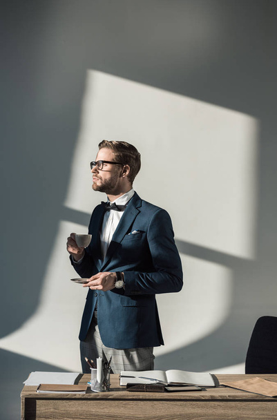 stylish young businessman in eyeglasses drinking coffee at workplace - Foto, afbeelding