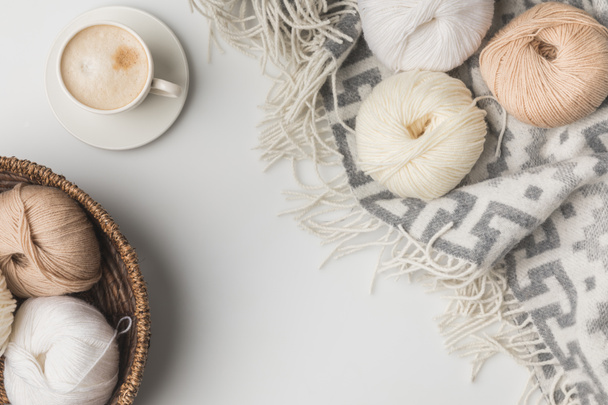 top view of yarn balls in wicker basket, cup of coffe and blanket on white background - Photo, Image