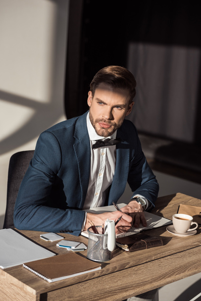 stylish young businessman writing in diary and looking away - 写真・画像