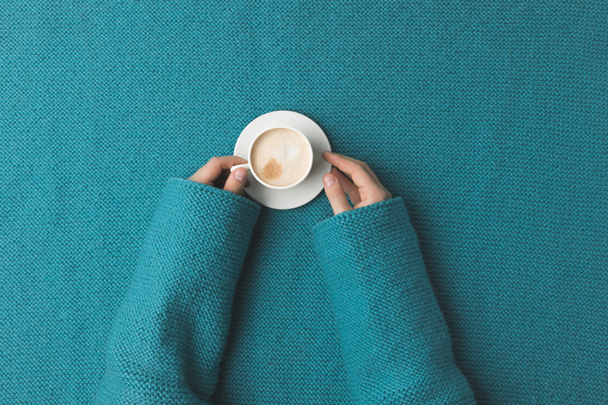 cropped view of woman hands with cup of coffee laying over turquoise fabric  - Photo, Image