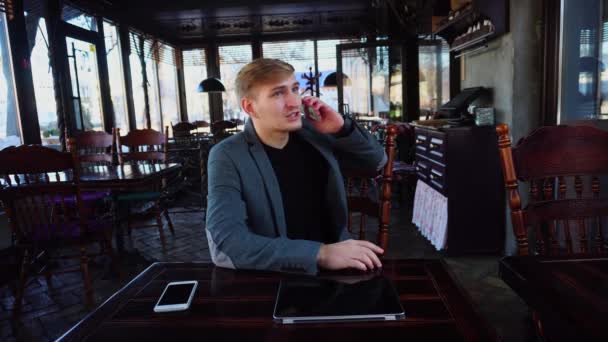 Empresário sentado perto da mesa com smartphone e laptop falando no telefone
 - Filmagem, Vídeo