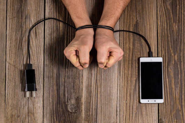 человеческие руки связаны с зарядкой телефона как символ зависимости от технологий и трудоголизма
 - Фото, изображение