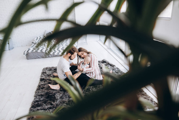 Mamá y papá pasan tiempo juntos con su linda hijita, sentados en la alfombra cerca de la ventana
 - Foto, imagen