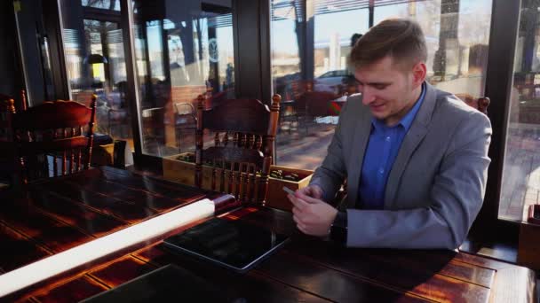 Biznesmen rozmowy w kawiarni przez smartfon w pobliżu tabletu. - Materiał filmowy, wideo