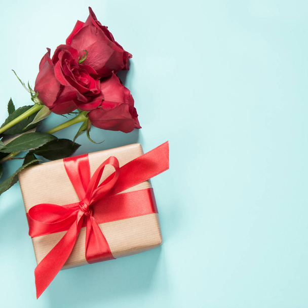 Bouquet of red roses and gift with red ribbon on pastel blue background. Valentine's card. Close up. Copy space. - Fotoğraf, Görsel