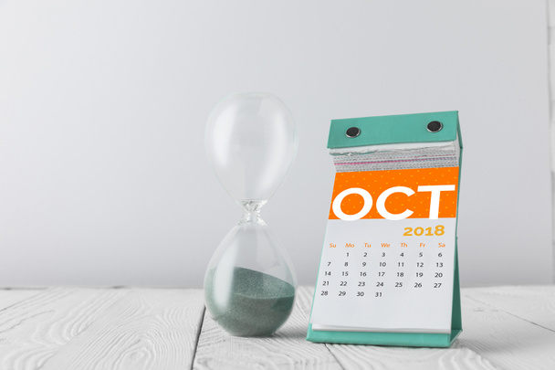 close up view of hourglass and october calendar on wooden tabletop isolated on white - Fotografie, Obrázek