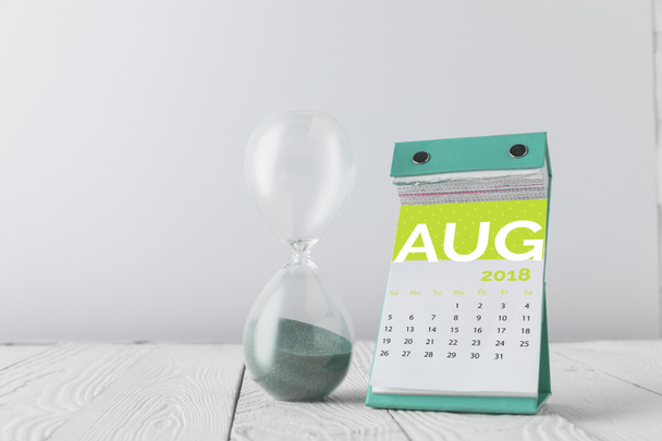 Nahaufnahme der Sanduhr und des Augustkalenders auf Holztischplatte isoliert auf Weiß - Foto, Bild