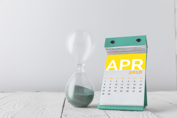 close up view of hourglass and april calendar on wooden tabletop isolated on white - Foto, afbeelding