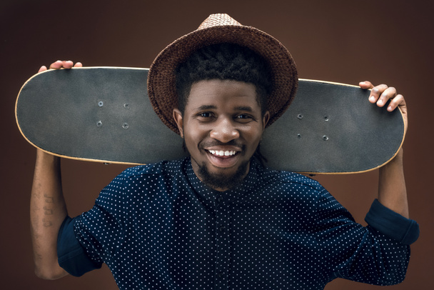 smiling african american man with skate isolated on brown - Foto, Imagem