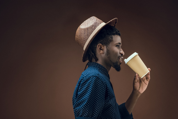 Afrika kökenli Amerikalı adam izole kahverengi üzerine kahve içme yan görünüm - Fotoğraf, Görsel
