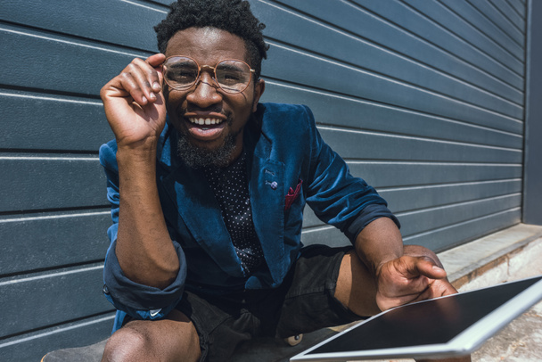 souriant élégant homme afro-américain en veste bleue tenant la tablette et regardant la caméra
 - Photo, image