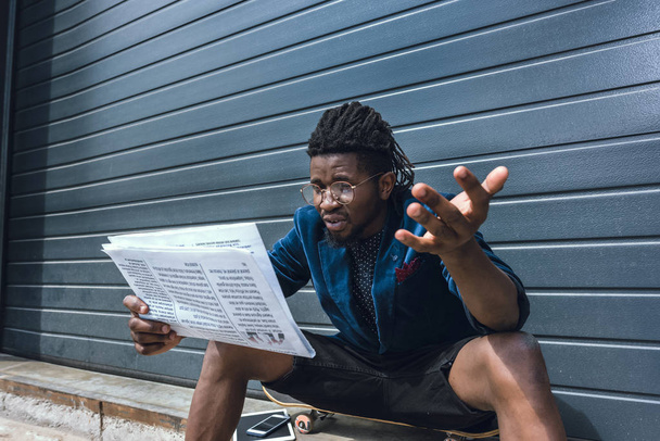шокований стильний афроамериканський чоловік у блакитній куртці читає газету
 - Фото, зображення