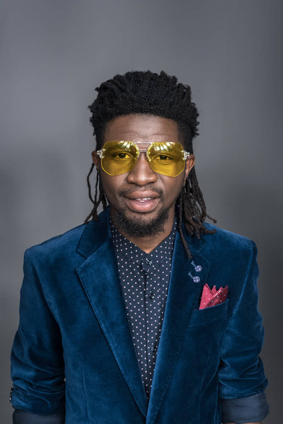 handsome african american man in yellow sunglasses and blue jacket isolated on gray - Foto, immagini