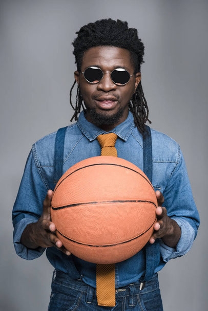 handsome african american man in black sunglasses holding basketball ball isolated on gray - Foto, Imagen