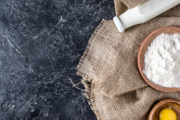 vista superior de botella de leche, yema y harina sobre tela de saco sobre mesa de mármol oscuro
 - Foto, Imagen