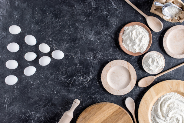 top view of raw eggs, flour, wooden plates, spoons and rolling pin for bakery on marble surface - 写真・画像