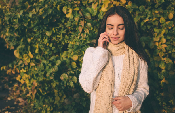 Woman using smartphone in fall. Autumn girl having smart phone conversation in sun flare foliage. Portrait of Caucasian model in forest in fall colors - Φωτογραφία, εικόνα