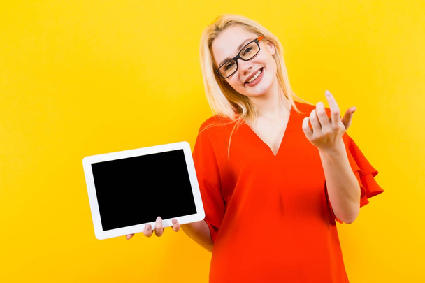Beautiful young woman in red dress posing with tablet PC on yellow background - Foto, Imagem