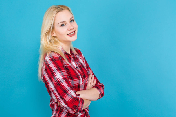 Studio portrait of beautiful young woman in red checkered shirt on blue background - Fotó, kép