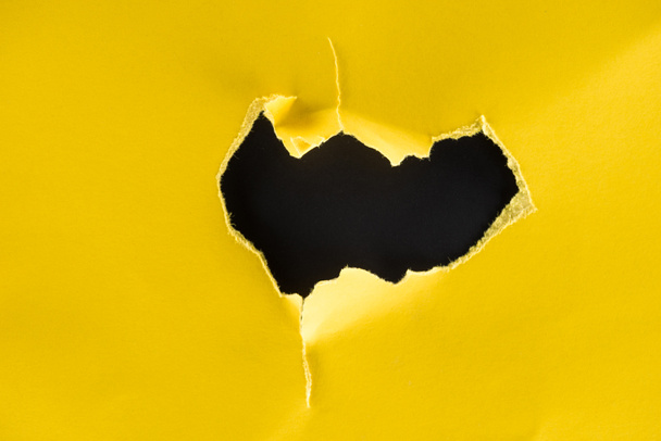 close-up shot of hole in yellow paper isolated on black - Foto, immagini