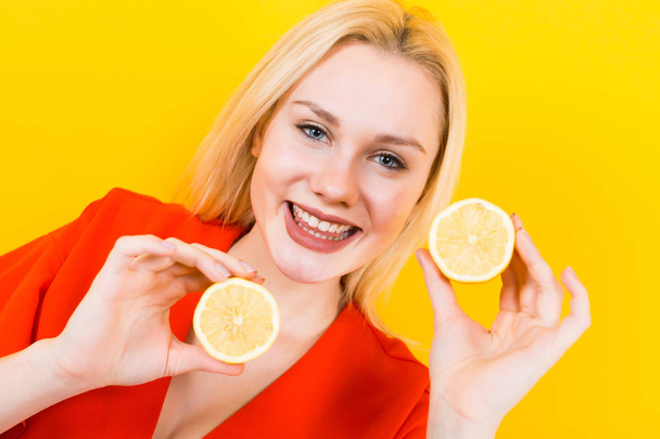 Beautiful young woman in red dress posing with lemon halves on yellow background - Фото, зображення